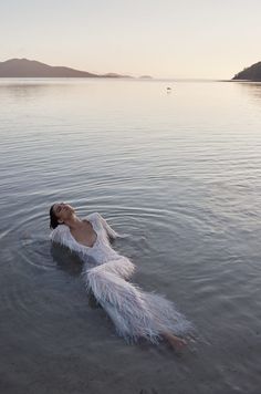 a woman is floating in the water with her arms spread out and she's wearing a white feathered dress