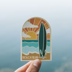 a person holding up a sticker with a surfboard in the middle of it