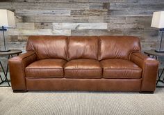 a brown leather couch sitting on top of a carpeted floor next to two lamps