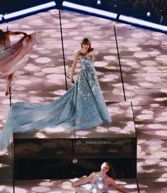 two women in gowns on stage with one woman laying down and the other standing up