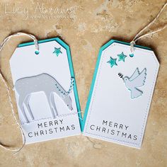 two christmas tags with an elephant and bird hanging from the top, on a stone surface