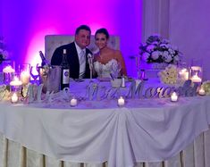 a bride and groom are sitting at a table with candles on it, posing for the camera