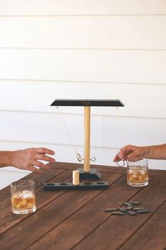 two people are playing with some sort of device on a wooden table, and one person is holding something in the other hand