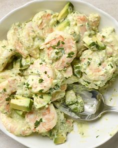 a white bowl filled with shrimp and cucumber salad next to a silver spoon