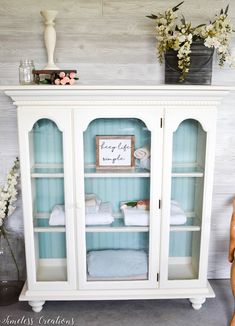 a white china cabinet with towels and flowers on top