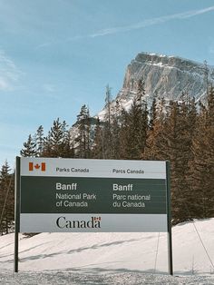 a sign in the snow with trees and mountains behind it that says banff, banff national park, parc national du canada