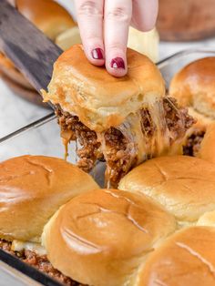 a person is picking up some pulled pork sliders from the baking pan with cheese on top