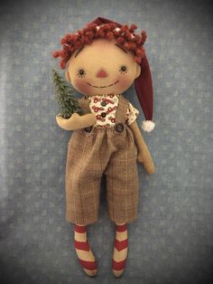 a doll with red hair is holding a small christmas tree in her hands and wearing brown overalls