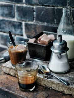 there are two drinks on the table with spoons and salt shakers next to it