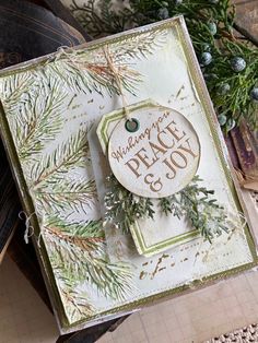 a close up of a christmas card on a table with pine cones and evergreen branches