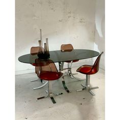 a glass table with four chairs around it and a vase on the top, in front of a white wall