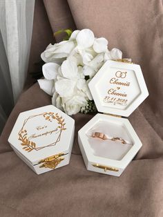 three wedding rings are sitting in small boxes next to white flowers on a brown cloth