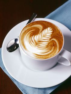 a cappuccino on a white saucer with a spoon and blue napkin