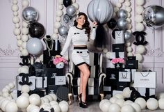 a woman sitting on a chair in front of balloons and boxes with black and white decorations