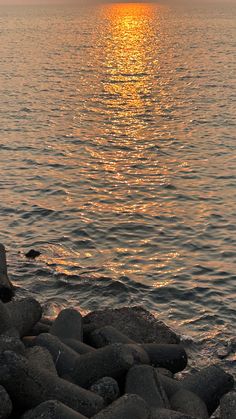 the sun is setting over the water and rocks