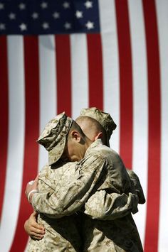 two soldiers hugging each other in front of an american flag