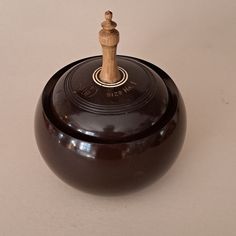 a small wooden figure sitting on top of a brown pot with lid and handle in the shape of a man