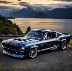 an old muscle car parked on the side of a road next to water and mountains