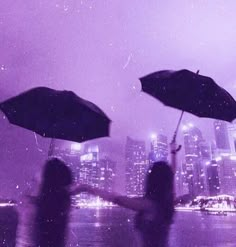 two people holding umbrellas in the rain with city lights and buildings in the background