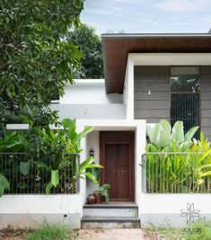 a house that has some plants in front of it and trees around the entrance door