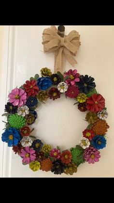 a wreath hanging on the front door with flowers and pinecones attached to it