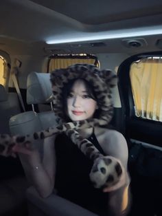 a woman wearing a leopard print hat and holding a stuffed animal in the back of a car