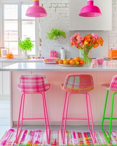 two pink and green chairs sitting in front of a kitchen island with flowers on it