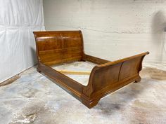 a wooden bed frame sitting on top of a cement floor next to a white brick wall