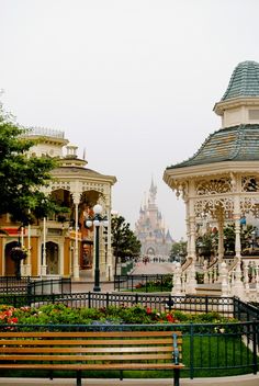 an empty park bench in front of a pavilion and other buildings with flowers on the ground