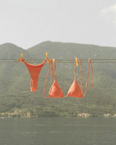 three orange bras hanging on a line over water