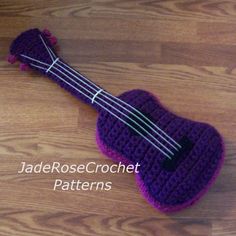 a purple crocheted ukulele sitting on top of a wooden floor