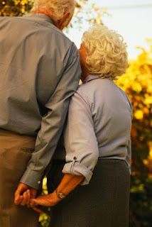 an older man and woman standing next to each other in front of trees with yellow leaves