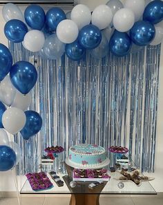 blue and white balloons are hanging from the ceiling above a cake on a table with cupcakes