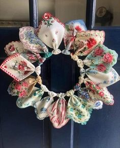 a wreath made out of cloths hanging on the front door with flowers and ribbons around it