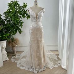 a wedding dress is displayed on a mannequin next to a potted plant