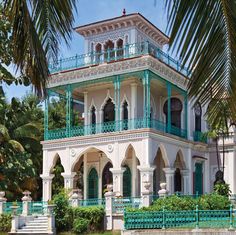 a large white and green building with balconies on the top floor, surrounded by palm trees