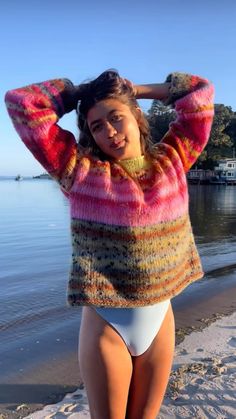 a woman standing on top of a beach next to the ocean wearing a colorful sweater