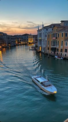 a boat is traveling down the water in front of some buildings at sunset or dawn