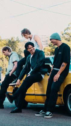 four young men sitting on the hood of a yellow car