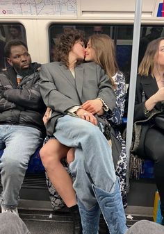 two people kissing while sitting on a subway train with other people in the back ground