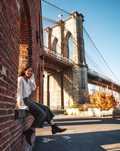 a woman leaning against a brick wall in front of the brooklyn bridge