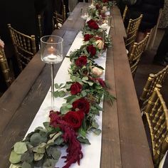 the long table is decorated with red flowers and greenery, along with wine glasses