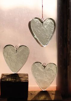 three heart shaped glass hangings on a window sill next to a wooden block