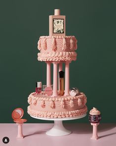 a three tiered cake with pink icing and decorations on the top, in front of a green background