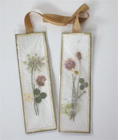 two framed pictures with flowers on them hanging from a brown ribbon tied to the wall