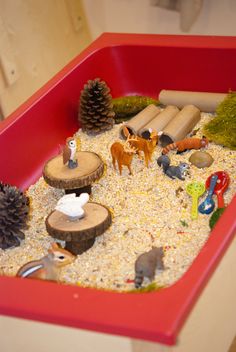 a red container filled with lots of different types of toy animals and trees in it