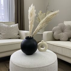 a black vase sitting on top of a white ottoman in a living room next to a couch