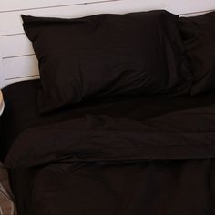 a bed with black sheets and pillows next to a night stand on a wooden floor