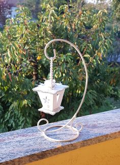 a white candle holder sitting on top of a wooden table next to some bushes and trees