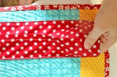 a person is holding a piece of fabric in front of a quilted pillow that has flowers on it